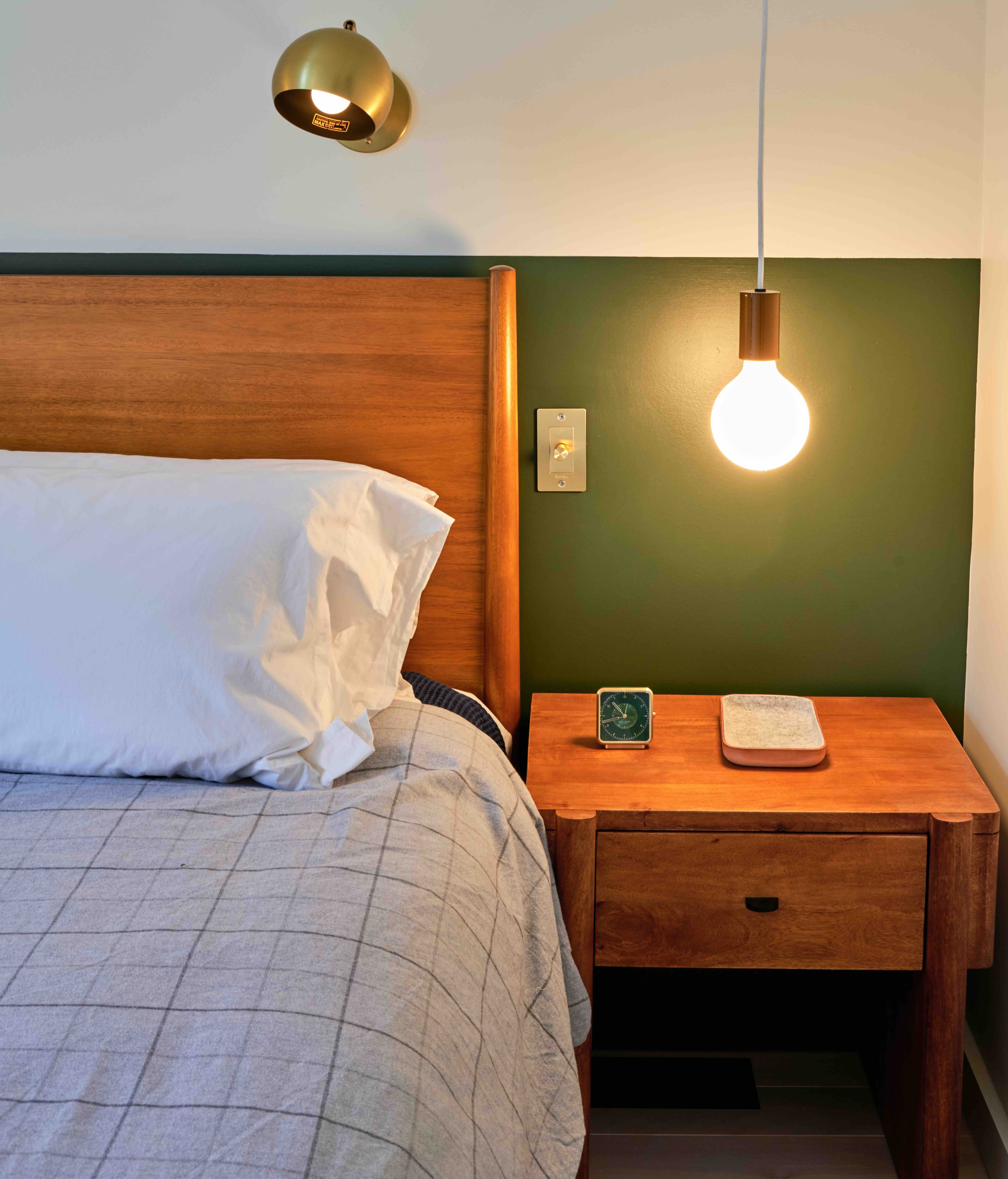 Primary bedroom detail — walnut headboard, brass sconce, and globe pendant against a forest-green accent wall