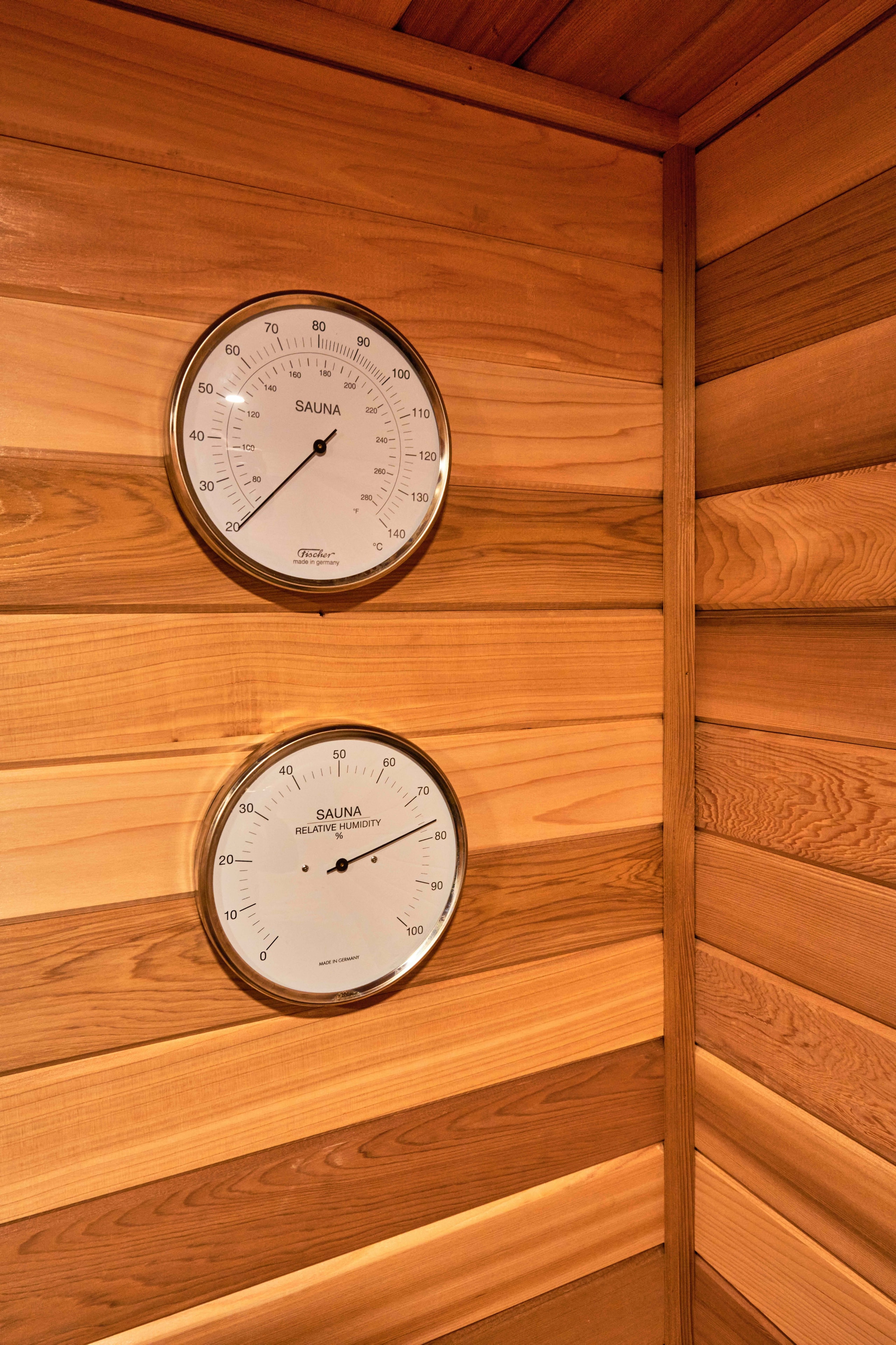 Cedar sauna thermometer and hygrometer gauges mounted on a tongue-and-groove wooden wall